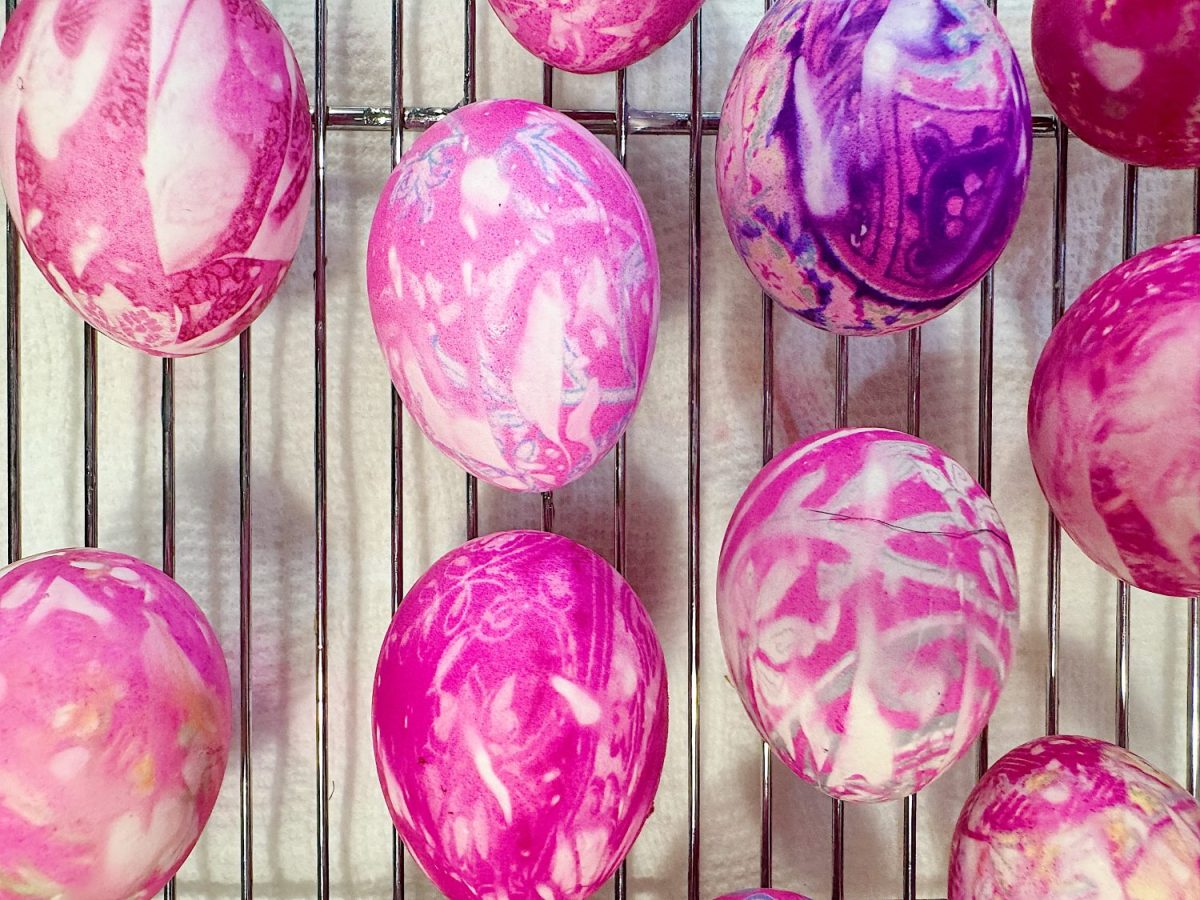 Pink and purple marbled eggs drying on a metal rack.