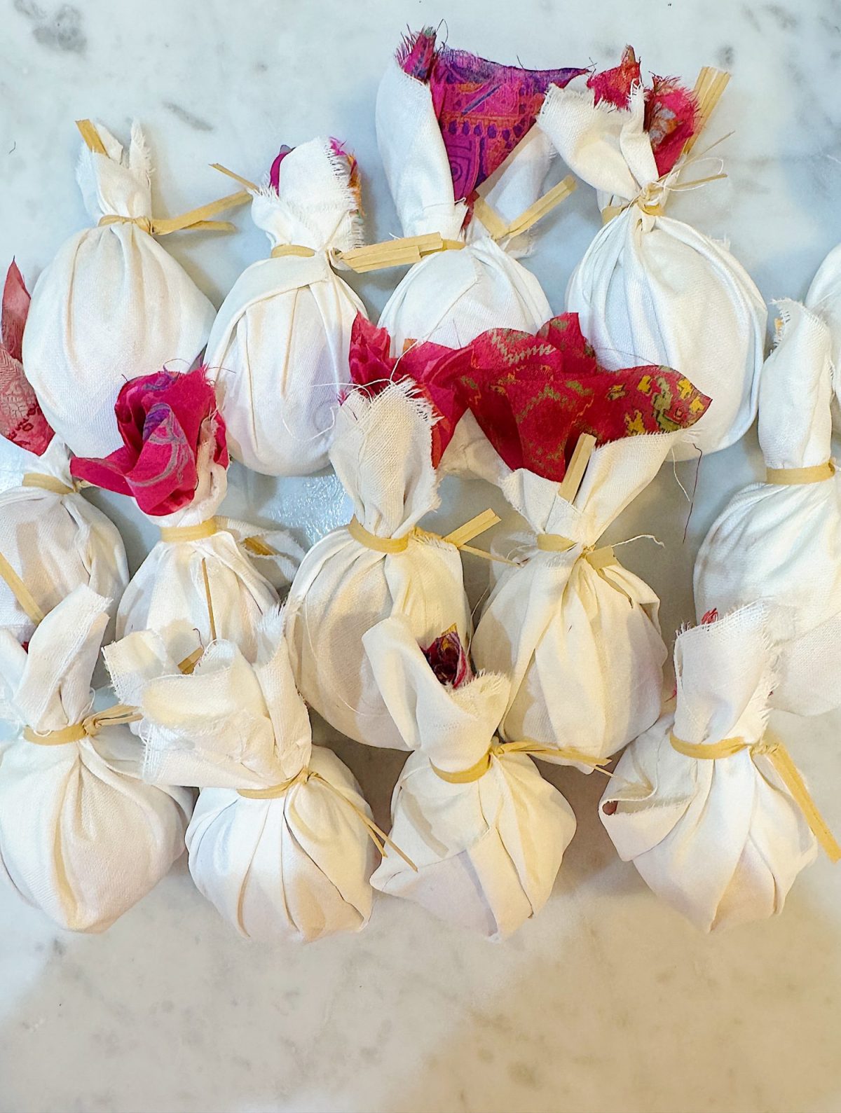 Small items wrapped in white fabric with colorful cloth accents, tied with string, arranged on a marble surface.