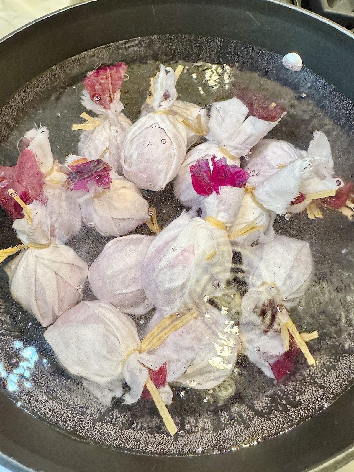 A pot filled with several fabric bundles tied with strings is being cooked in boiling water.