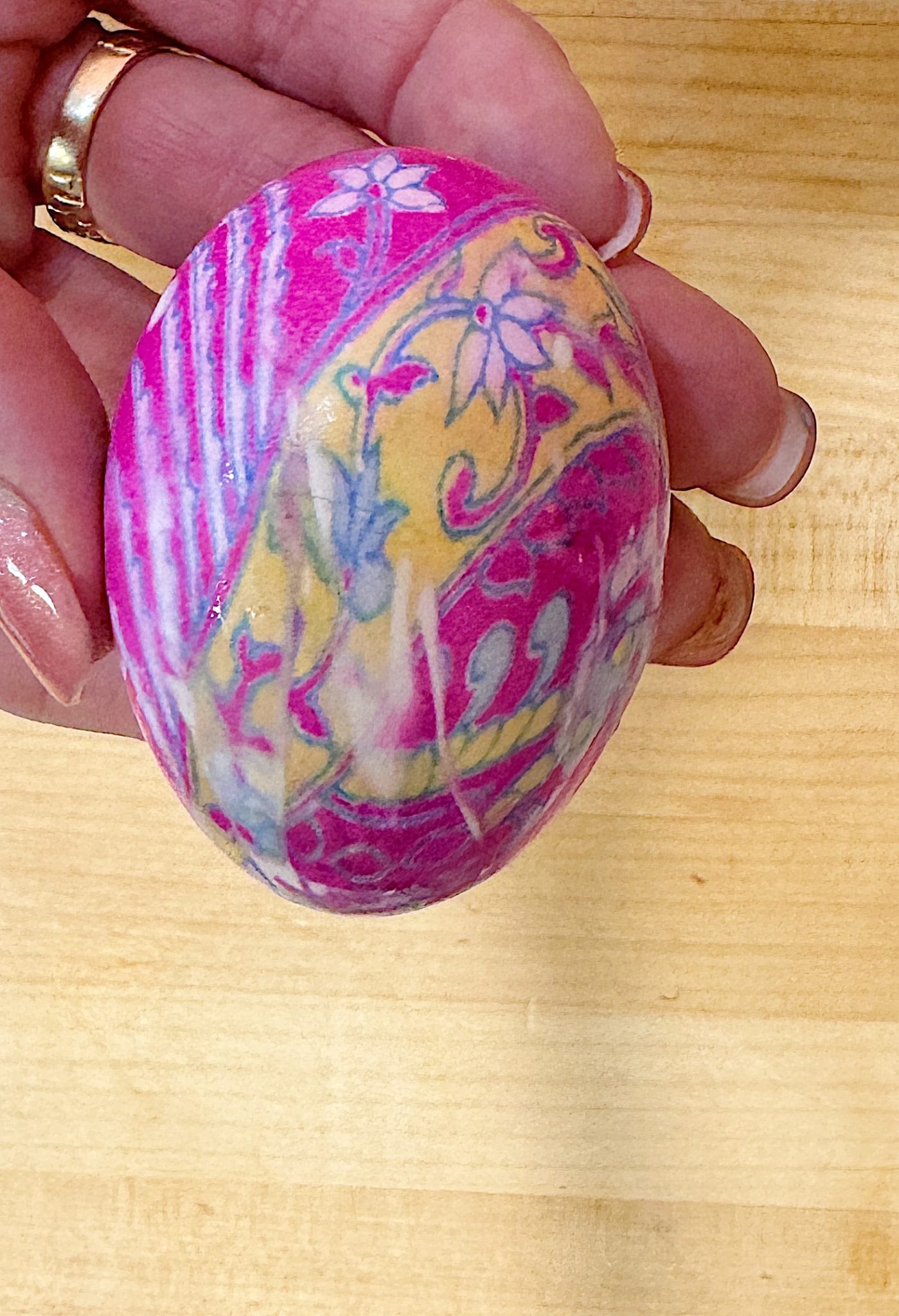 A hand holding a decorated egg with a pink, yellow, and white floral pattern.