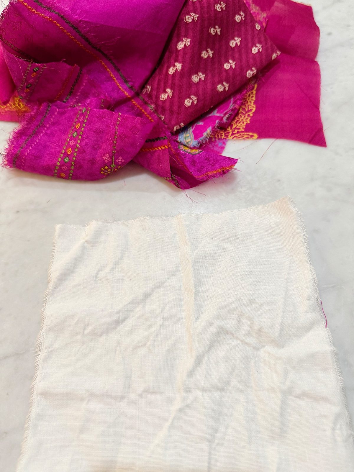 White fabric piece next to vibrant pink patterned fabric pieces on a white marble surface.
