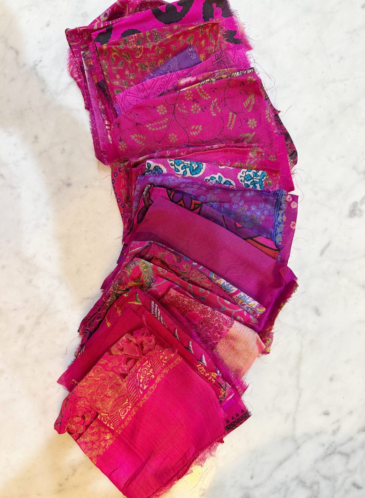 A stack of neatly folded, vibrant pink fabric squares with various patterns and textures on a marble surface.