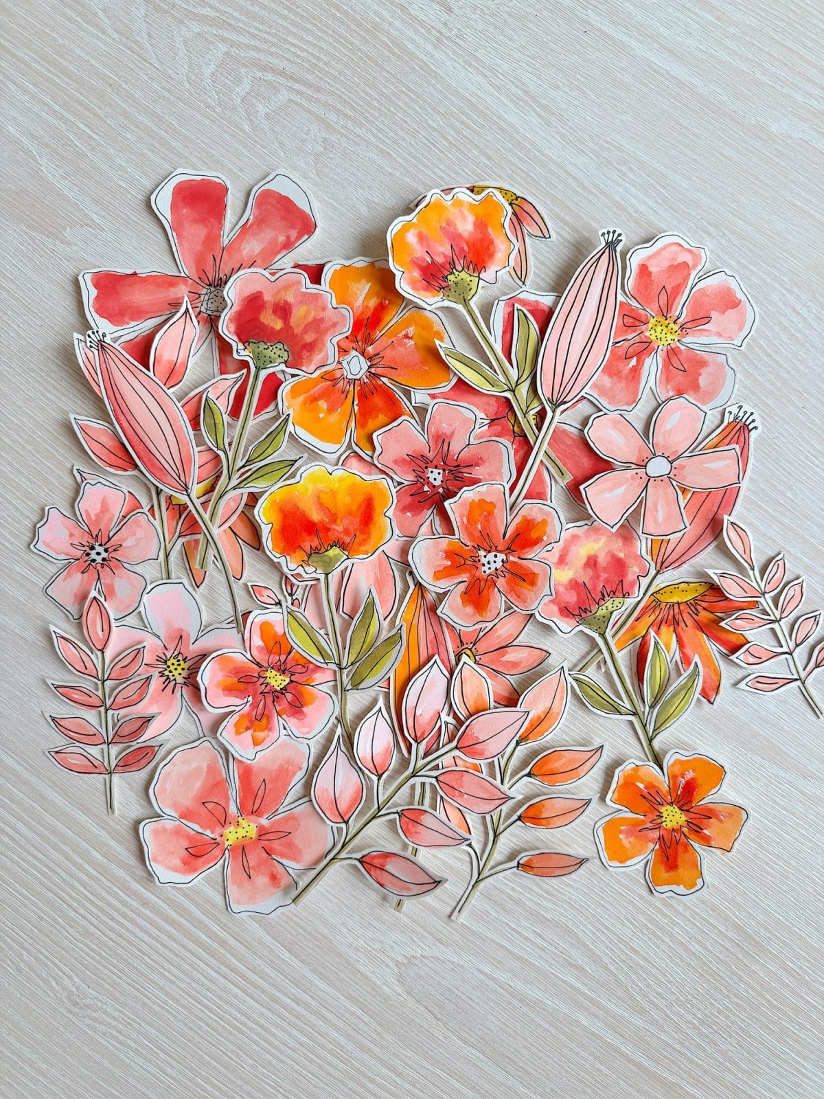 A collection of illustrated orange and pink flowers and leaves is arranged on a light wooden surface.