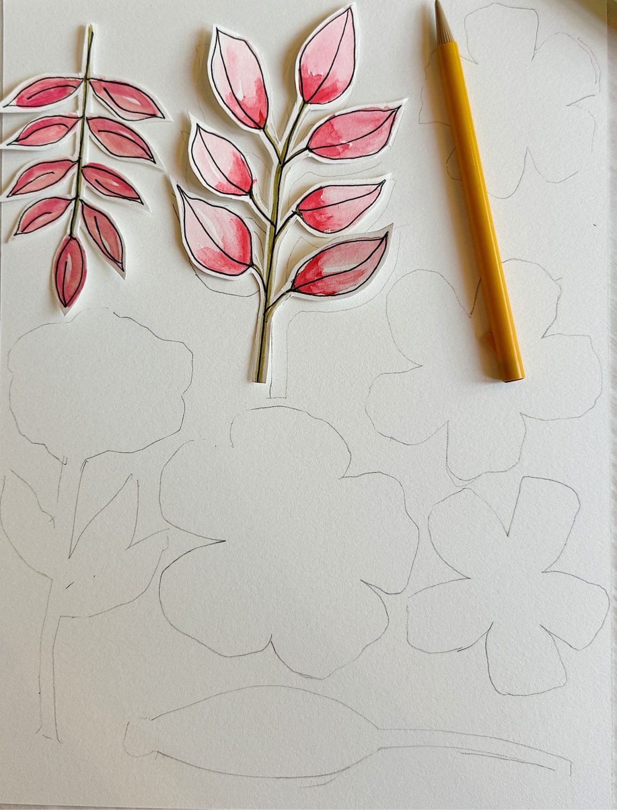 Cut-out watercolor drawings of pink leaves are placed on paper with pencil sketches of flowers and a yellow pencil lying beside them.