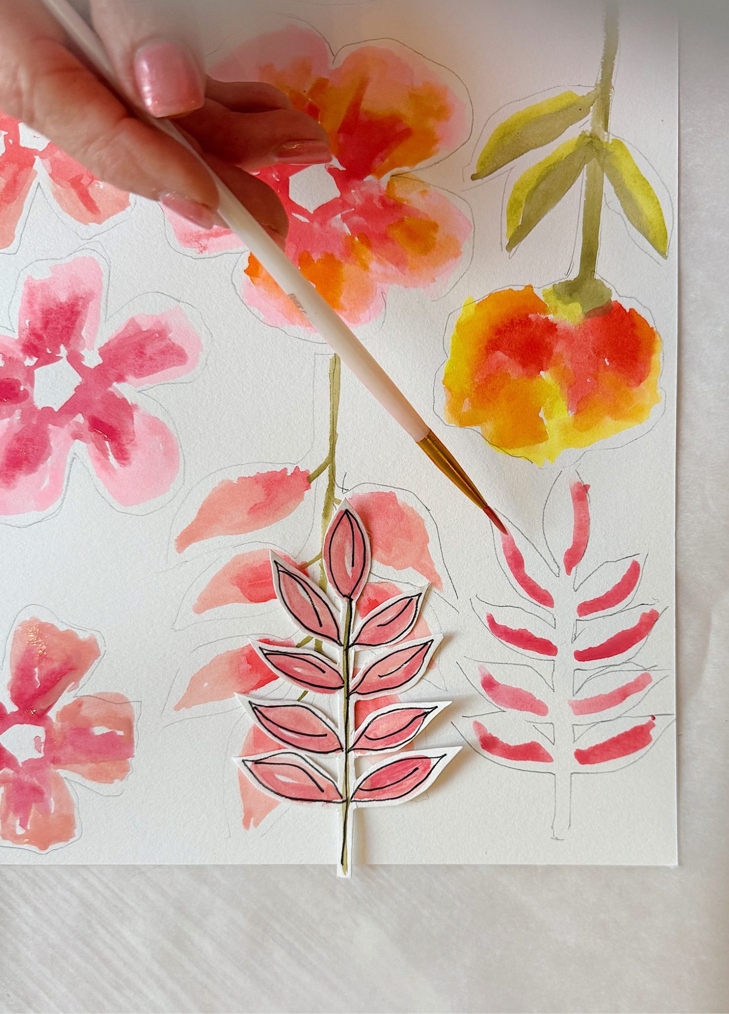 A hand holds a paintbrush, painting red and orange watercolor flowers and leaves on white paper; a cut-out leaf illustration is placed on top of the artwork.