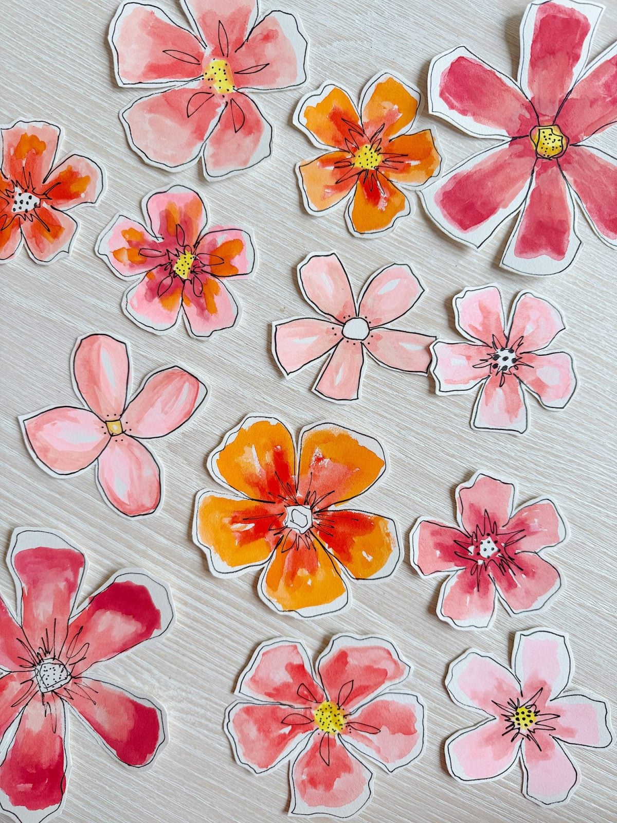 Cutout paper flowers in shades of red, pink, and orange with hand-drawn outlines are arranged on a light wooden surface.