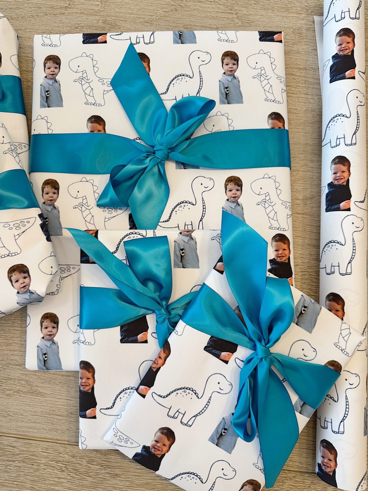 Gift boxes wrapped in paper featuring dinosaur drawings and child photos, adorned with bright blue ribbons.