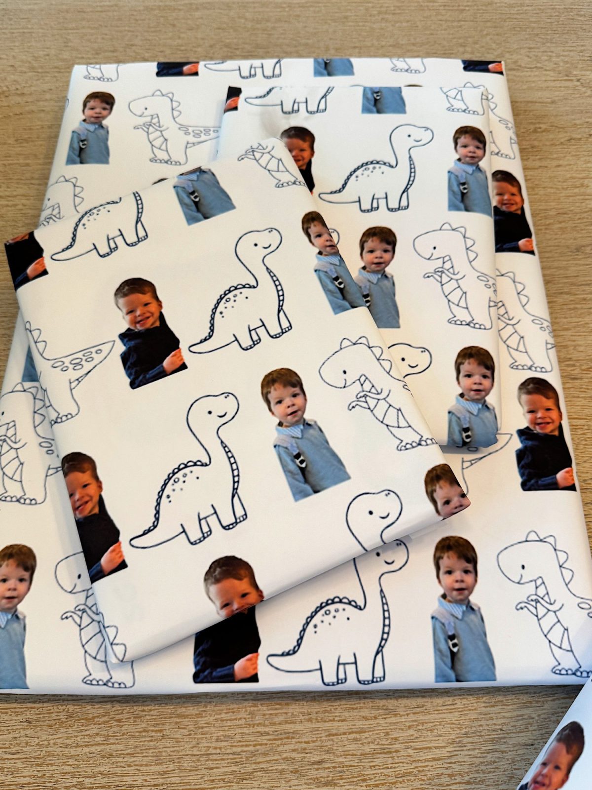 Gift wrapped in paper featuring dinosaur drawings and a child's photo on a light wood surface.