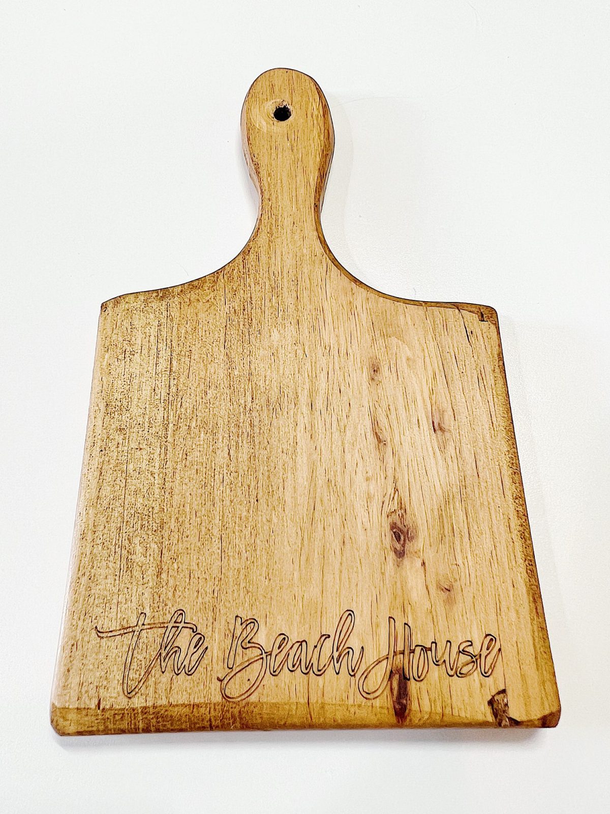 Wooden cutting board with a handle, featuring the engraved text "The Beach House" in cursive script.