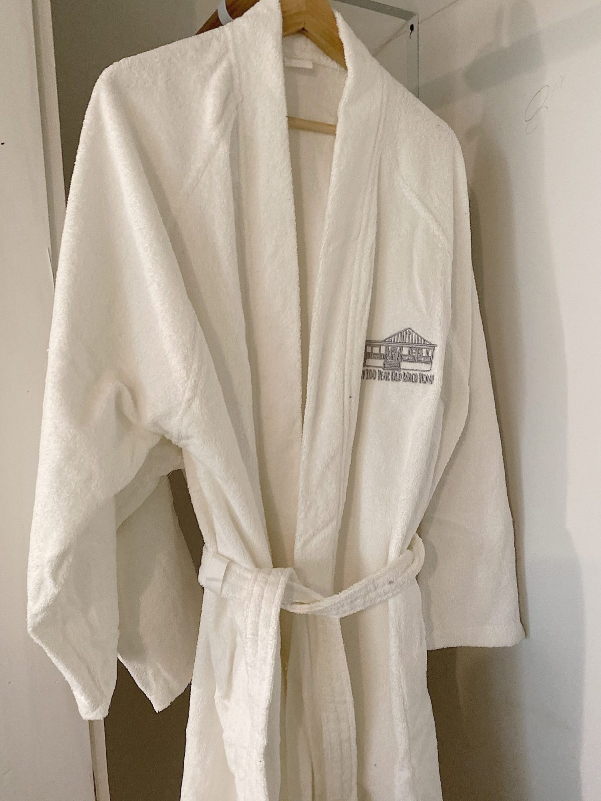 A white bathrobe hanging on a wall hook, with an embroidered logo on the chest.