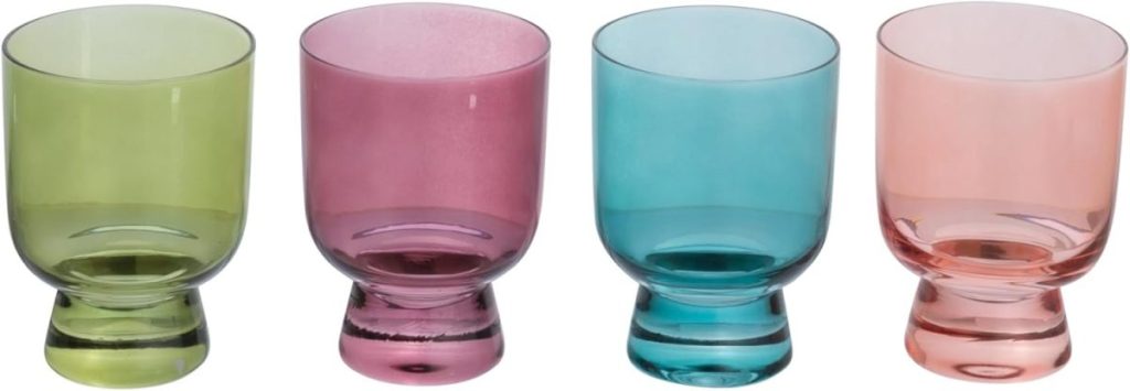 Four short, round drinking glasses in green, purple, blue, and pink are arranged in a row against a white background&mdash;perfect for serving vibrant summer mocktails.