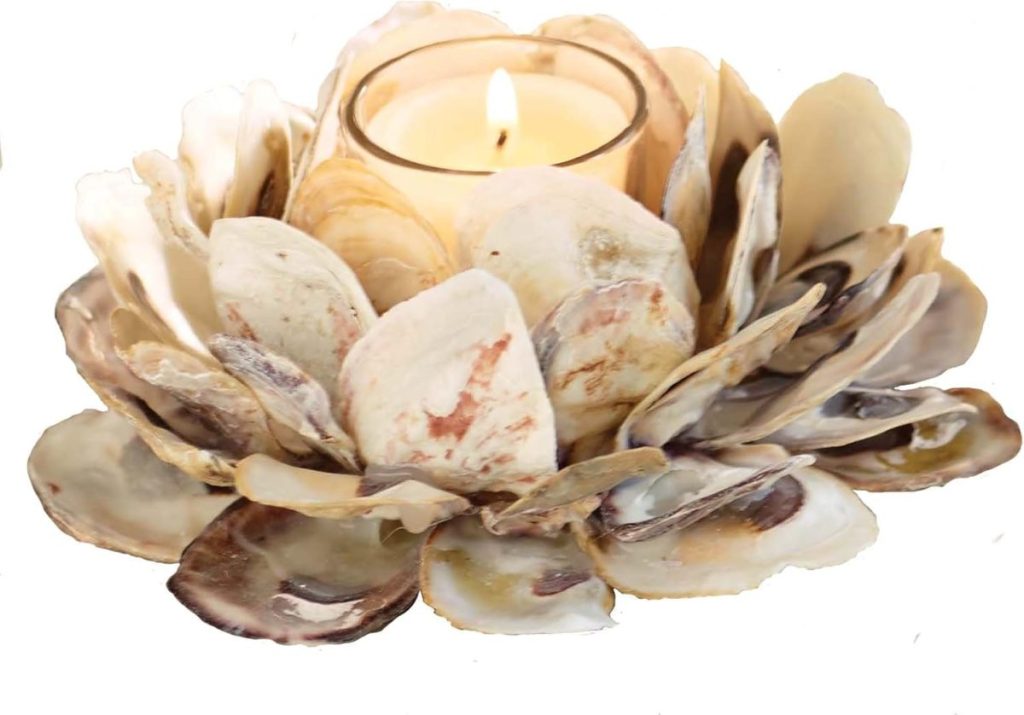 A lit tealight candle is placed in a holder made from layered seashells arranged in a circular flower-like pattern—perfect for summer decorating ideas.