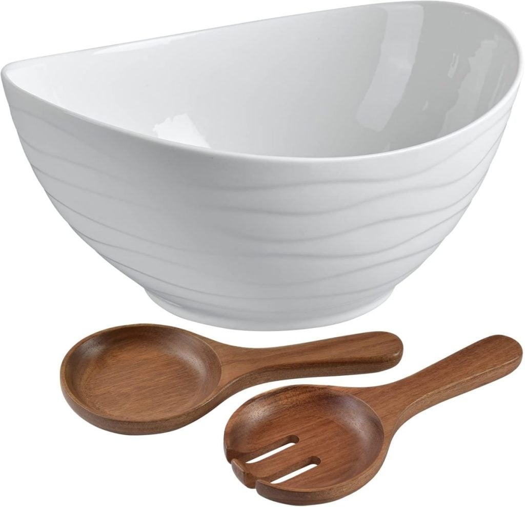 A white, oval ceramic salad bowl with subtle wavy patterns, accompanied by a wooden salad spoon and fork—perfect for elevating your salad bar ideas.