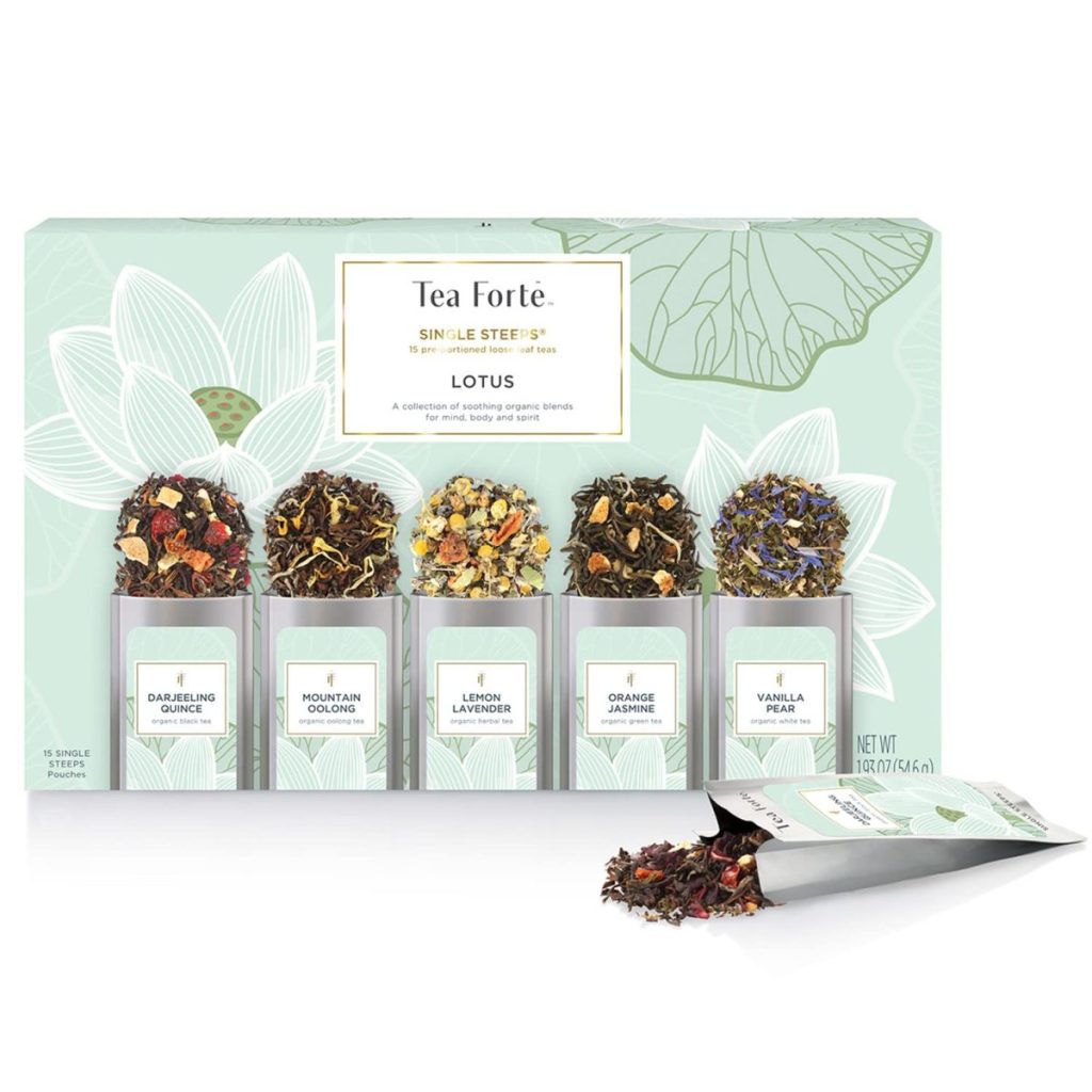 A box of Tea Fort&eacute; Lotus collection featuring five glass containers with different loose leaf teas, alongside tea bags and some loose tea spilling from an opened packet.