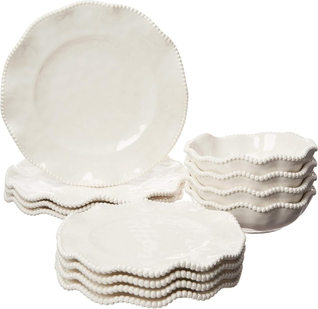 A set of white ceramic dinnerware featuring scalloped edges and raised beaded detailing, including plates and bowls&mdash;perfect for creating a stylish pool party tablescape&mdash;stacked on a white background.