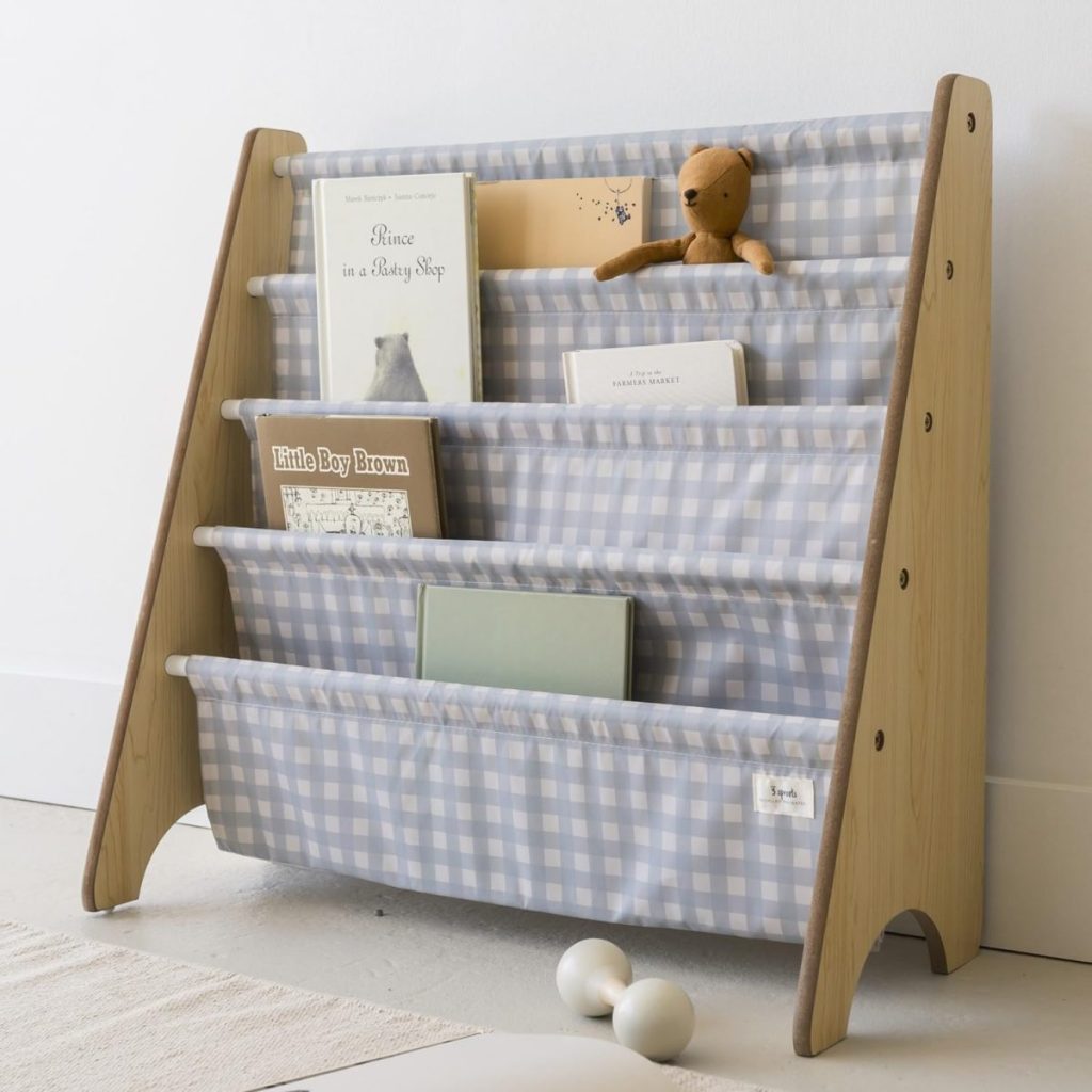 A small bookshelf with a blue-and-white checkered fabric holds children's books and a brown stuffed animal, standing on a light floor near a white wall—an adorable touch for summer decorating ideas in any child's room.