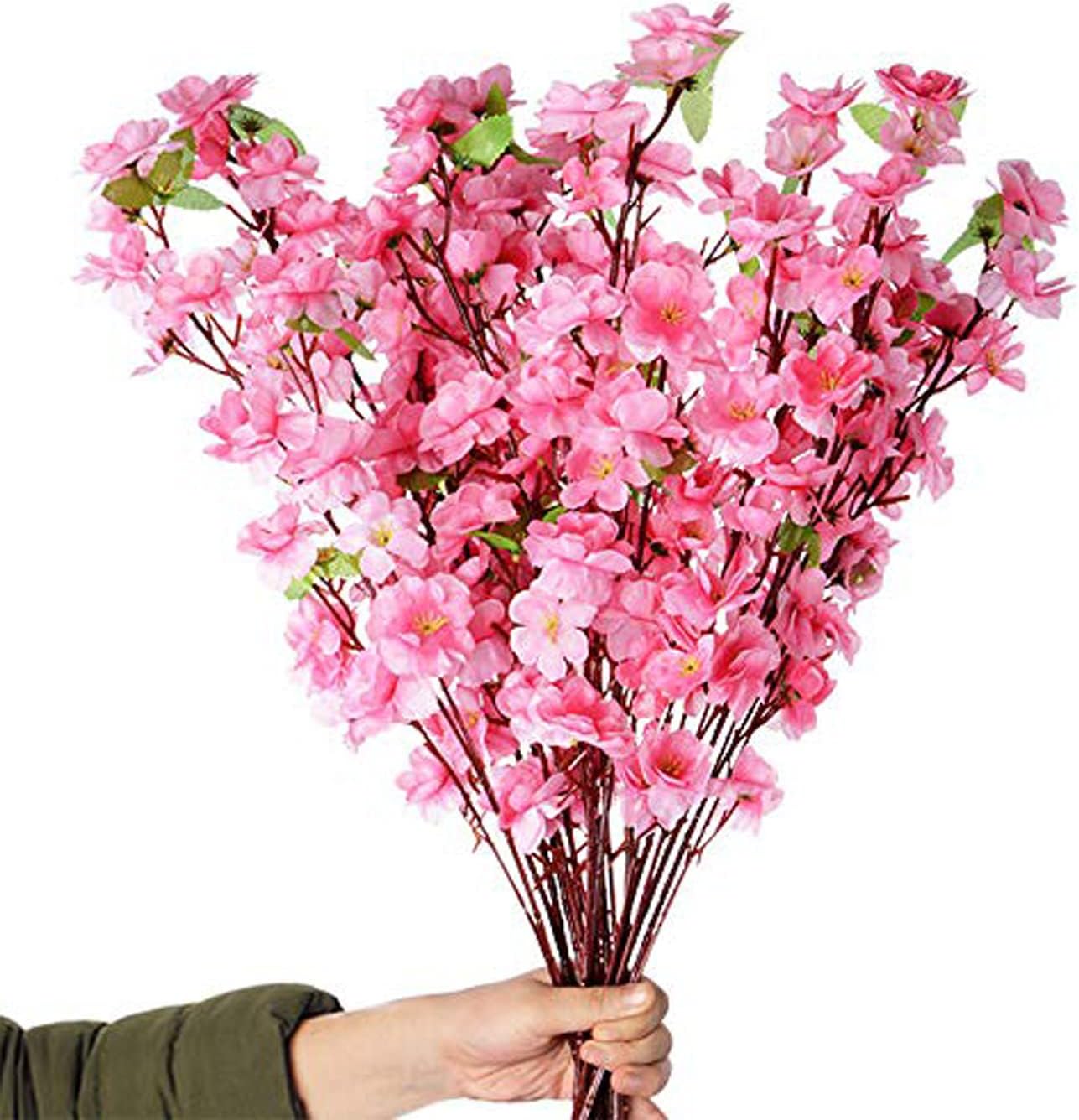 A hand holds a large bouquet of artificial pink cherry blossom branches with green leaves, perfect for creating stunning tablescapes, against a white background.