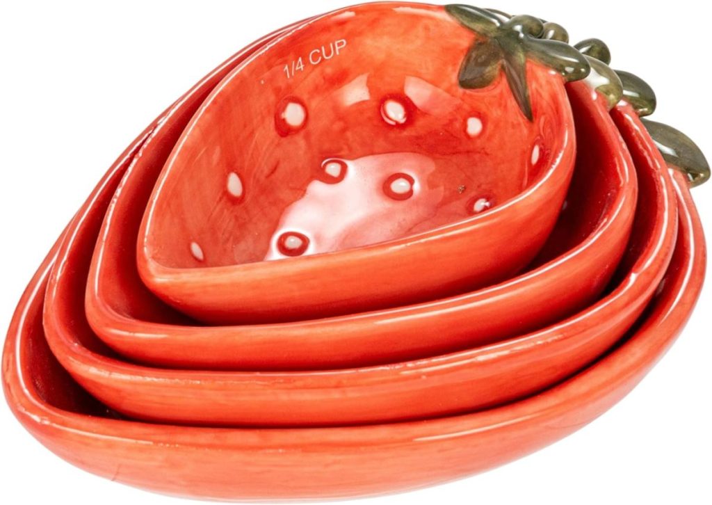 Set of four red ceramic measuring cups shaped like strawberries, nested together with painted green leaves on the handles—perfect for a mixed berry theme in your kitchen.