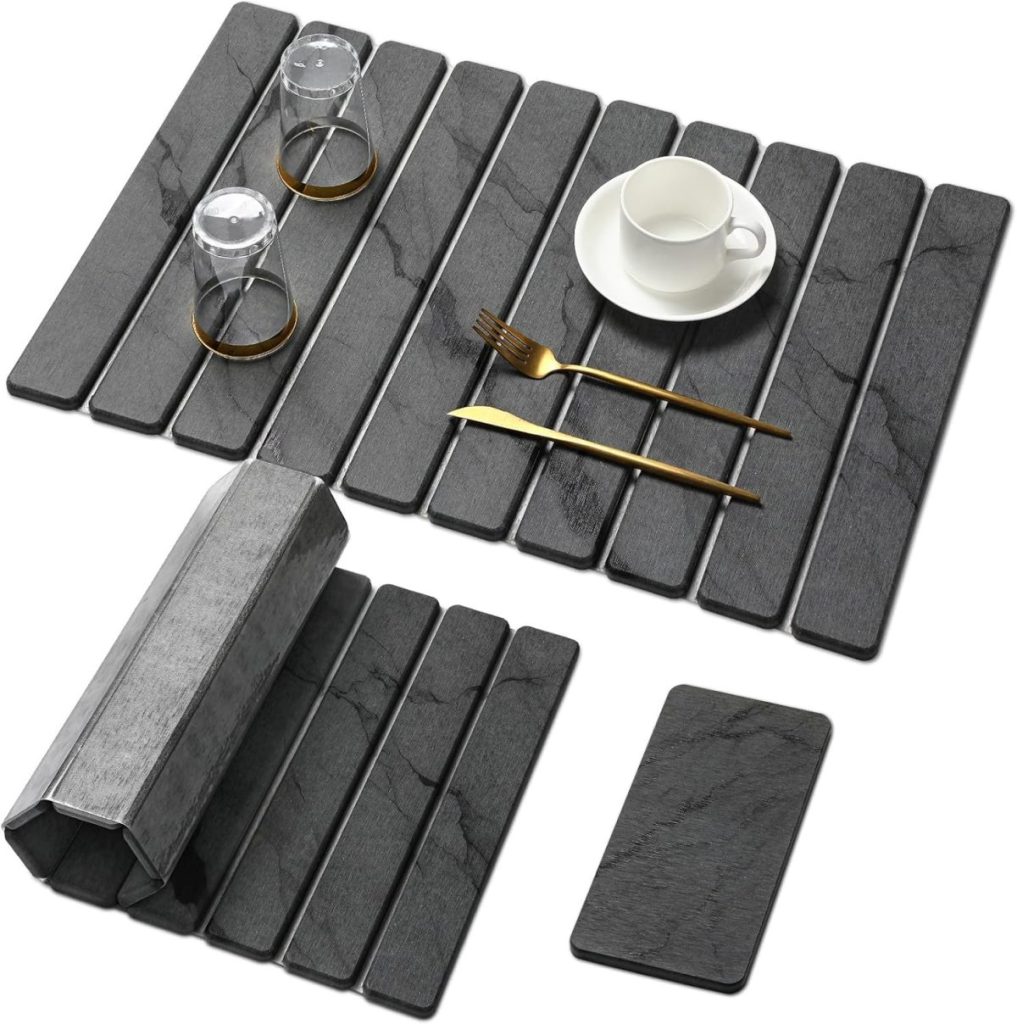 A set of dark gray rectangular placemats with a marble pattern, ideal for an open concept kitchen, holding two glasses, a cup and saucer, a fork, and knife; one placemat is rolled up and one stands alone.