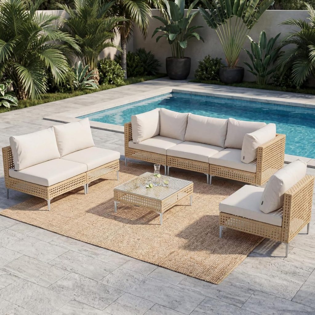 Outdoor patio set with beige outdoor cushions on sofas and a glass-top coffee table atop a woven rug beside a swimming pool, surrounded by tropical plants.