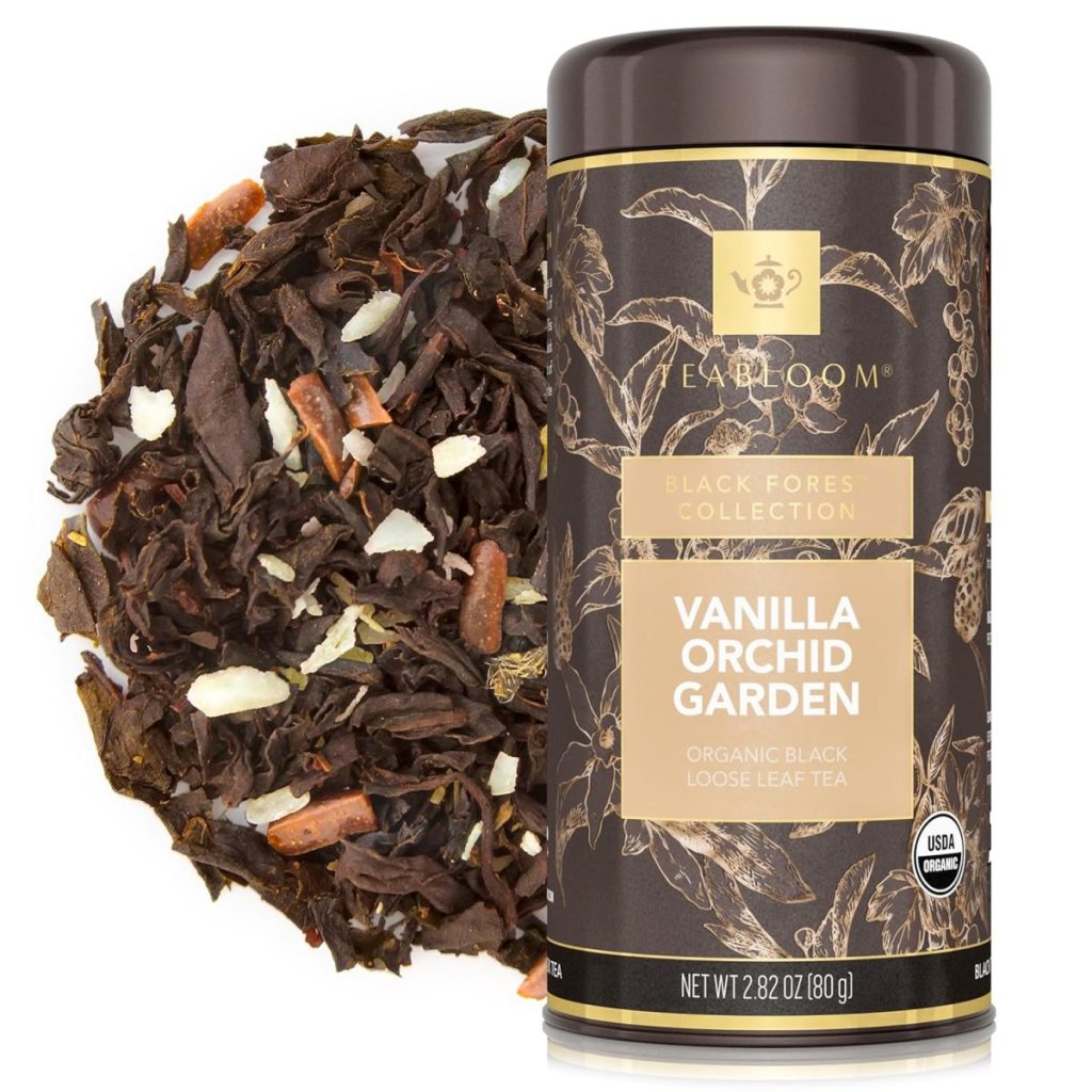 A container of EABLoom Vanilla Orchid Garden organic black loose leaf tea is shown next to a pile of loose tea leaves, visible ingredients, and a few tea bags for convenient brewing.