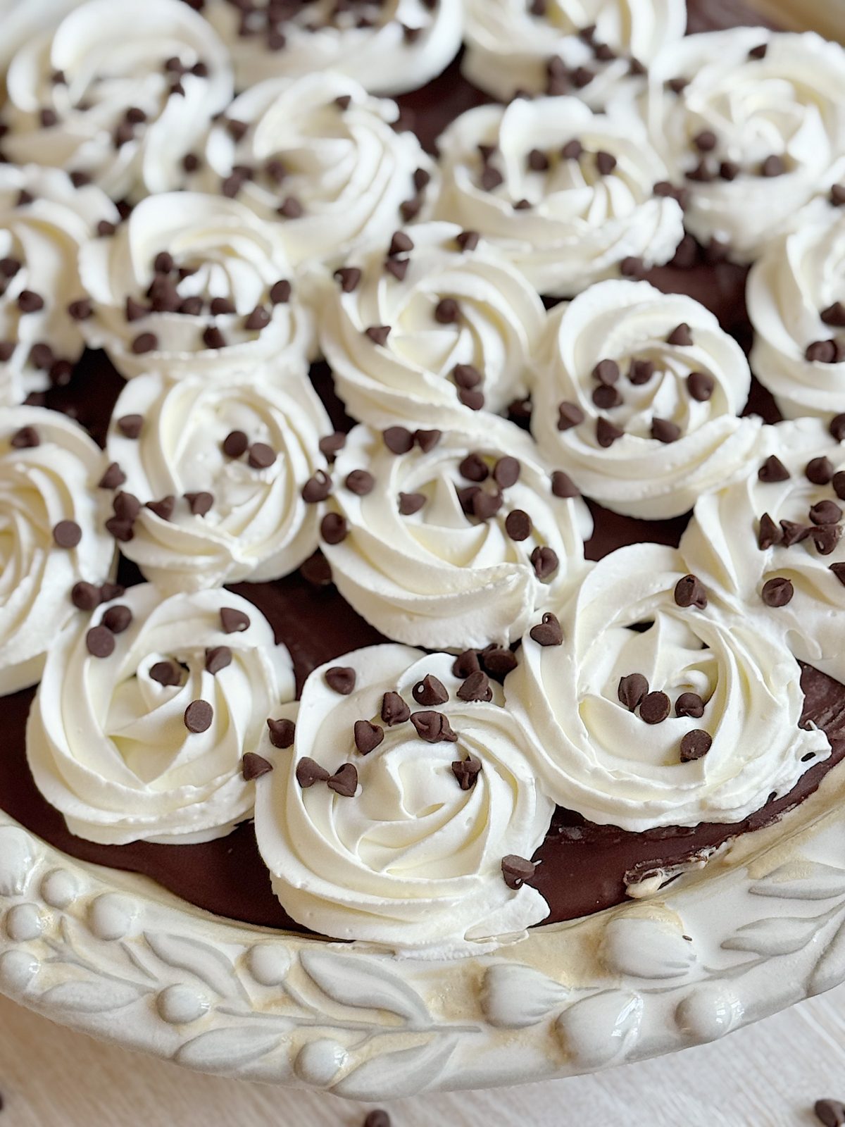 A chocolate pie topped with swirls of whipped cream and sprinkled with mini chocolate chips in a decorative pie dish.