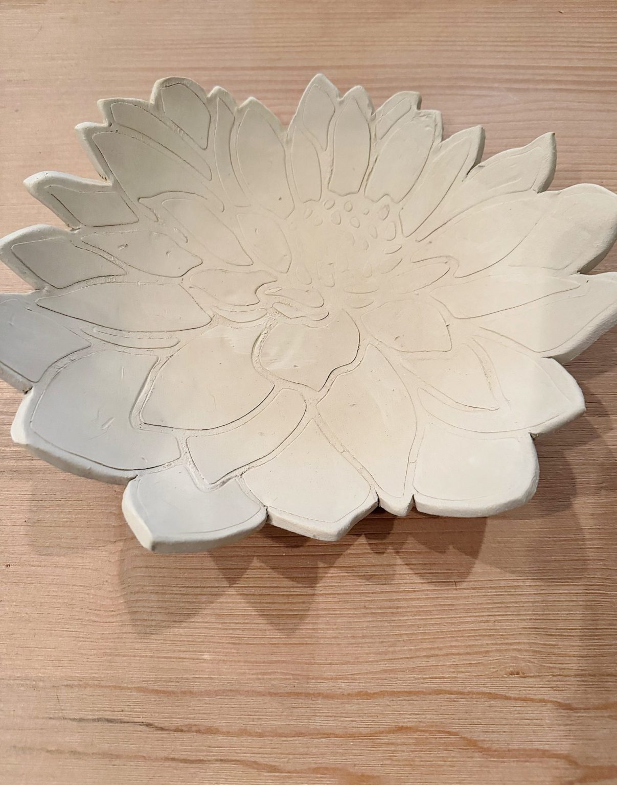 A white ceramic plate shaped and textured like a flower sits on a light wood surface.