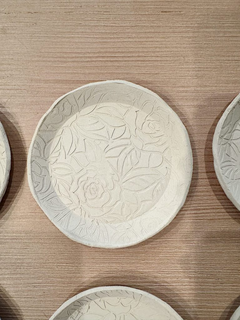 A round ceramic plate with a raised floral and leaf pattern, placed on a light wood surface.