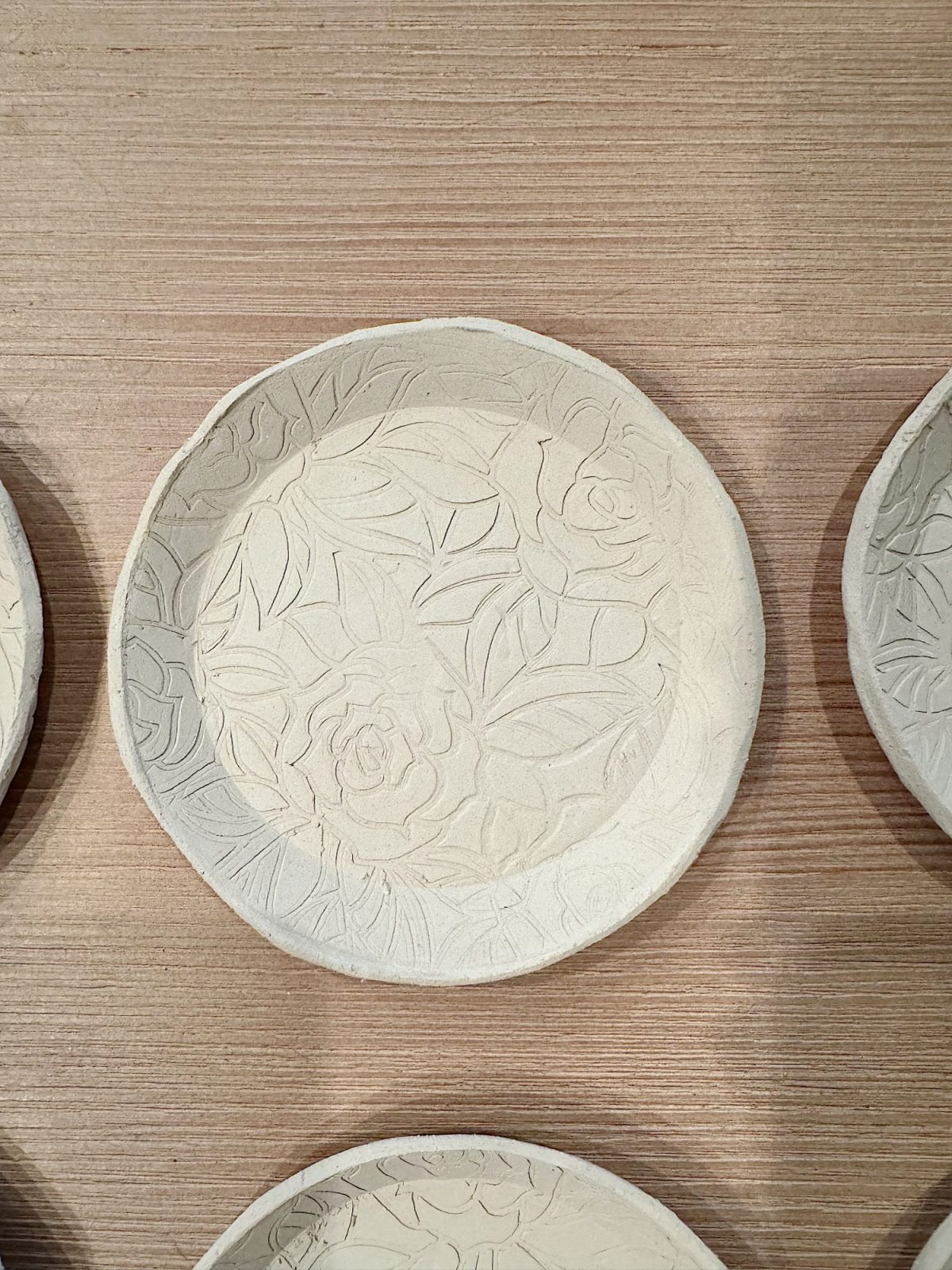 A round ceramic plate with a raised floral and leaf pattern, placed on a light wood surface.