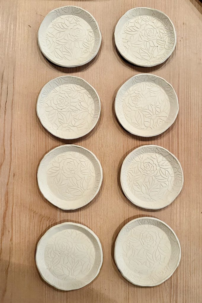 Eight small, round ceramic plates with floral patterns are arranged in two vertical columns on a wooden surface.