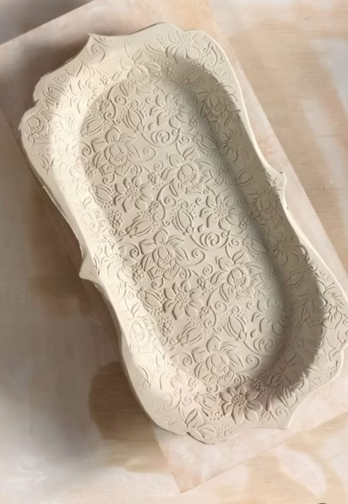 A rectangular ceramic tray with ornate, embossed floral patterns is displayed on a light wooden surface.