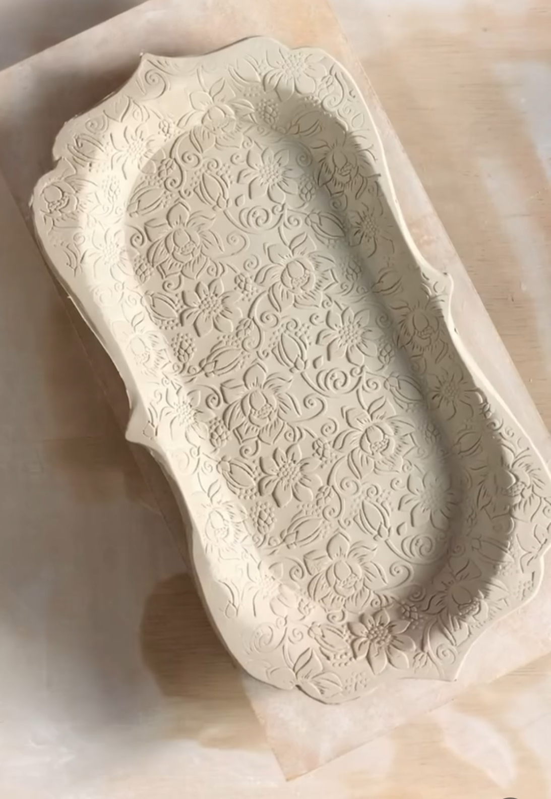 A rectangular ceramic tray with ornate, embossed floral patterns is displayed on a light wooden surface.