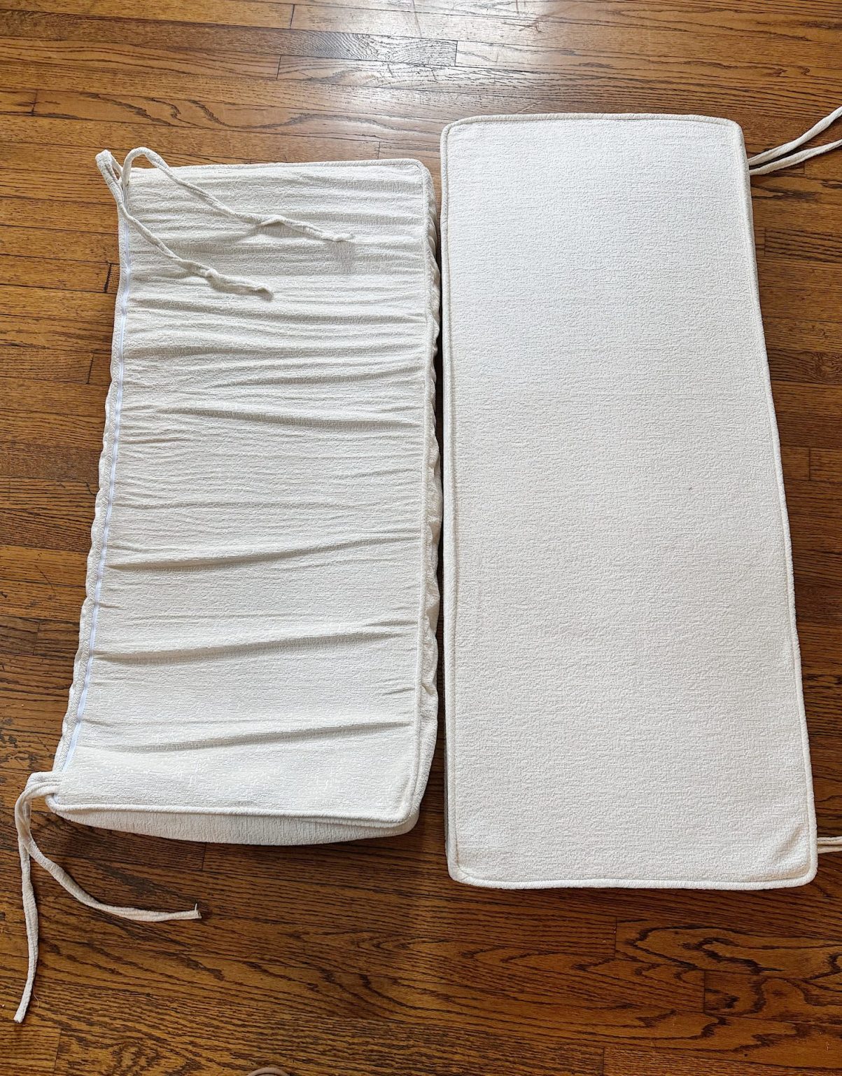 Two white rectangular seat cushions are placed side by side on a wooden floor; the left cushion is wrinkled while the right cushion appears smooth.