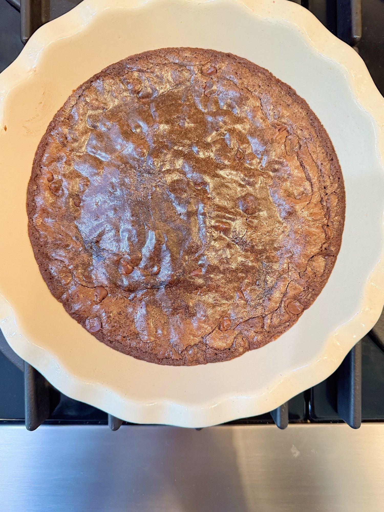 A round chocolate brownie baked in a cream-colored pie dish, resting on a stovetop.