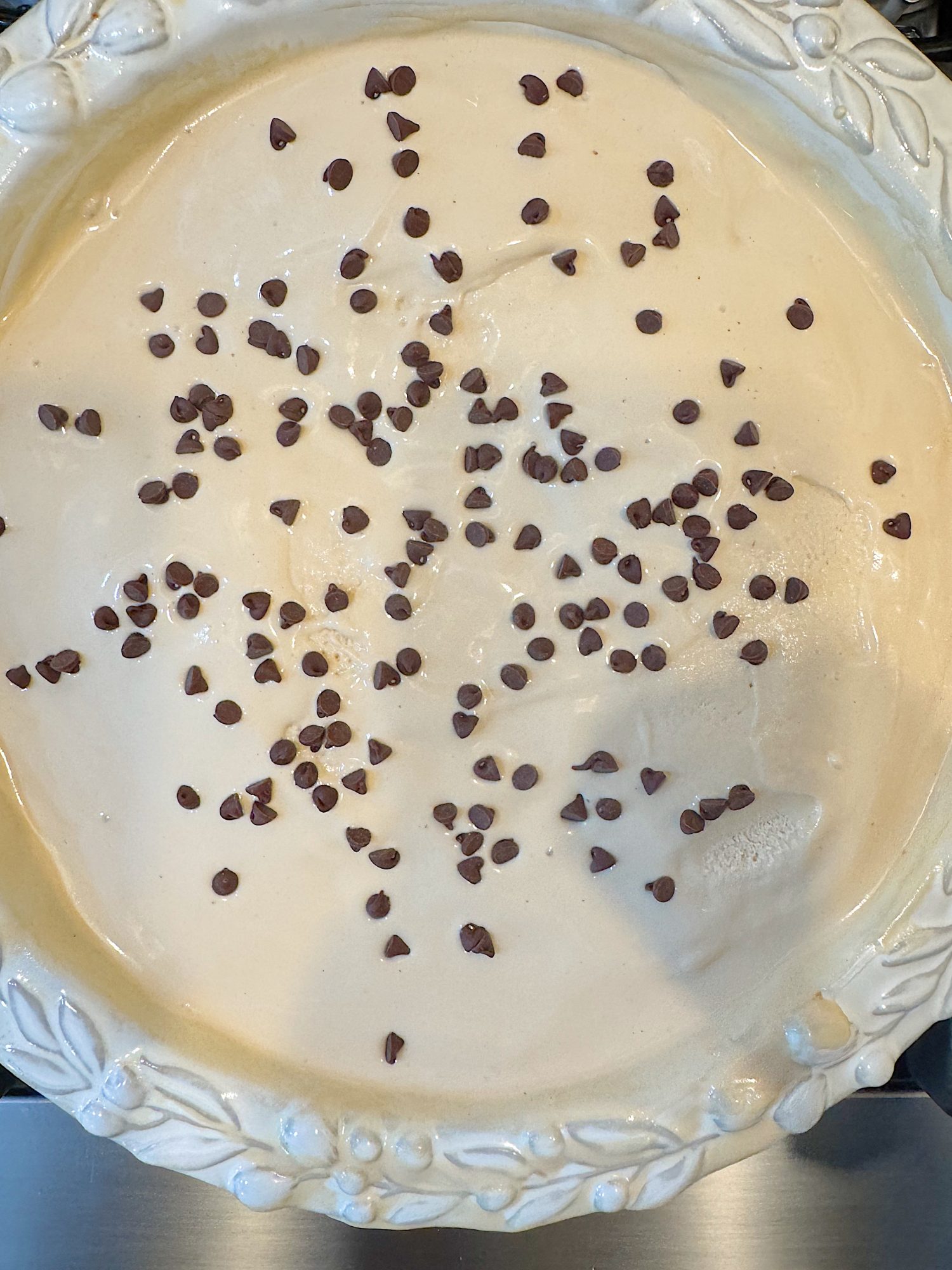 A pie with a creamy beige filling in a decorative dish, topped with scattered mini chocolate chips.