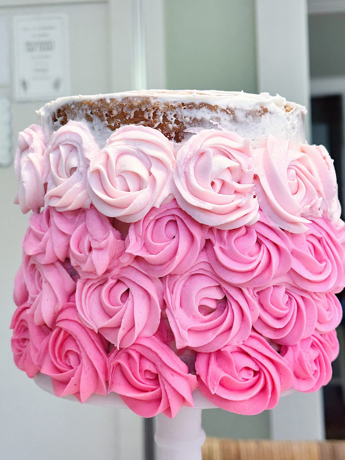 A cake decorated with pink and white rosette frosting, with the top part of the cake partially unfrosted, revealing the sponge underneath.