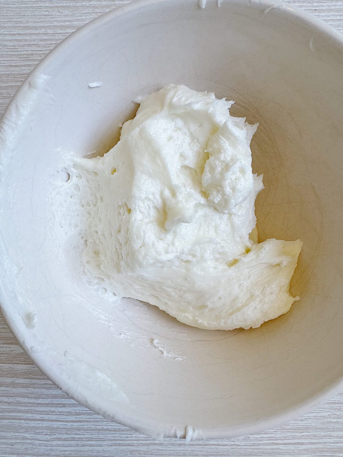 White, sticky dough rests in a large white mixing bowl on a light-colored wooden surface.