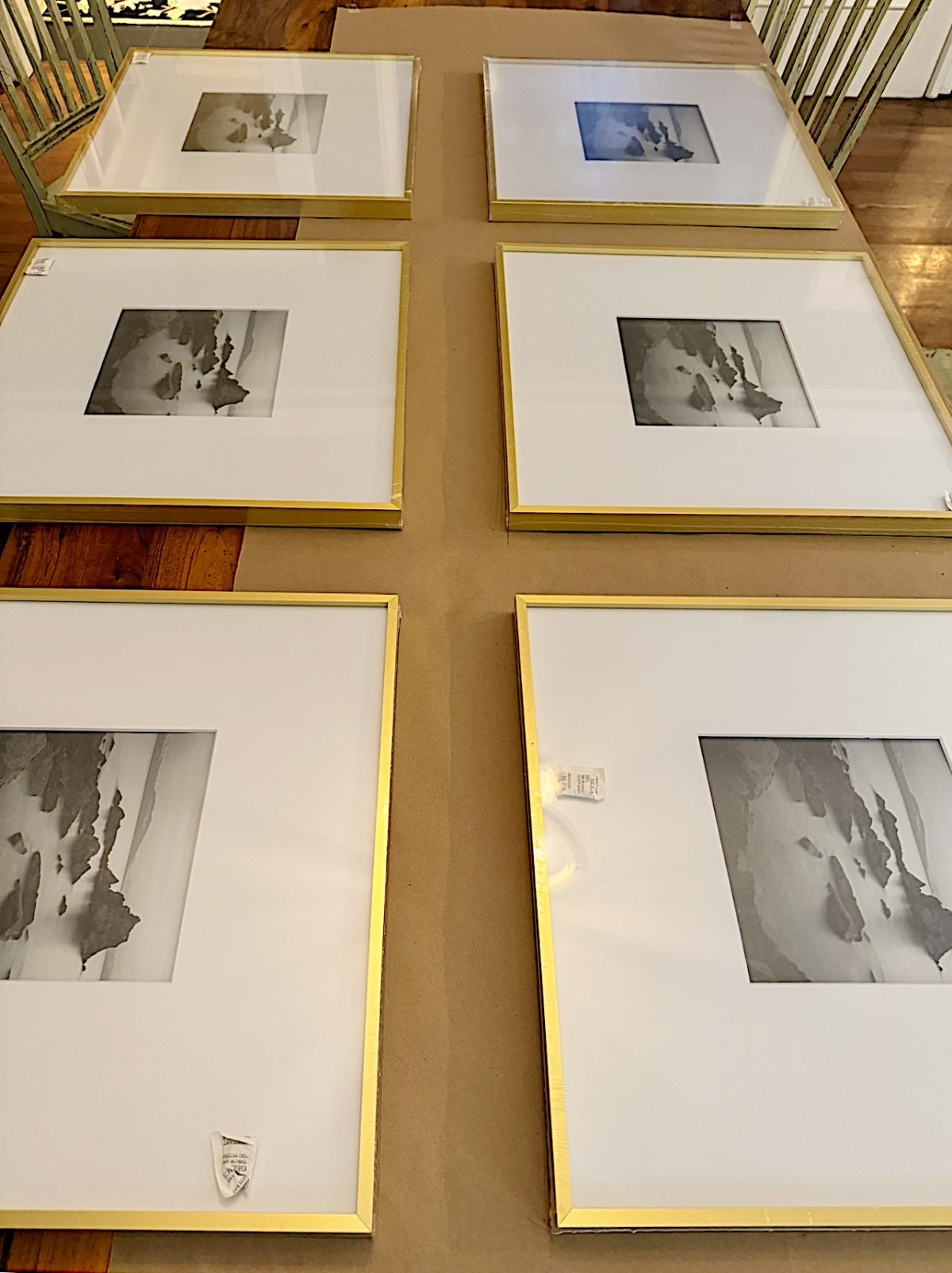 Six framed black-and-white landscape photographs with gold frames are laid out on a surface, possibly for arrangement or hanging.