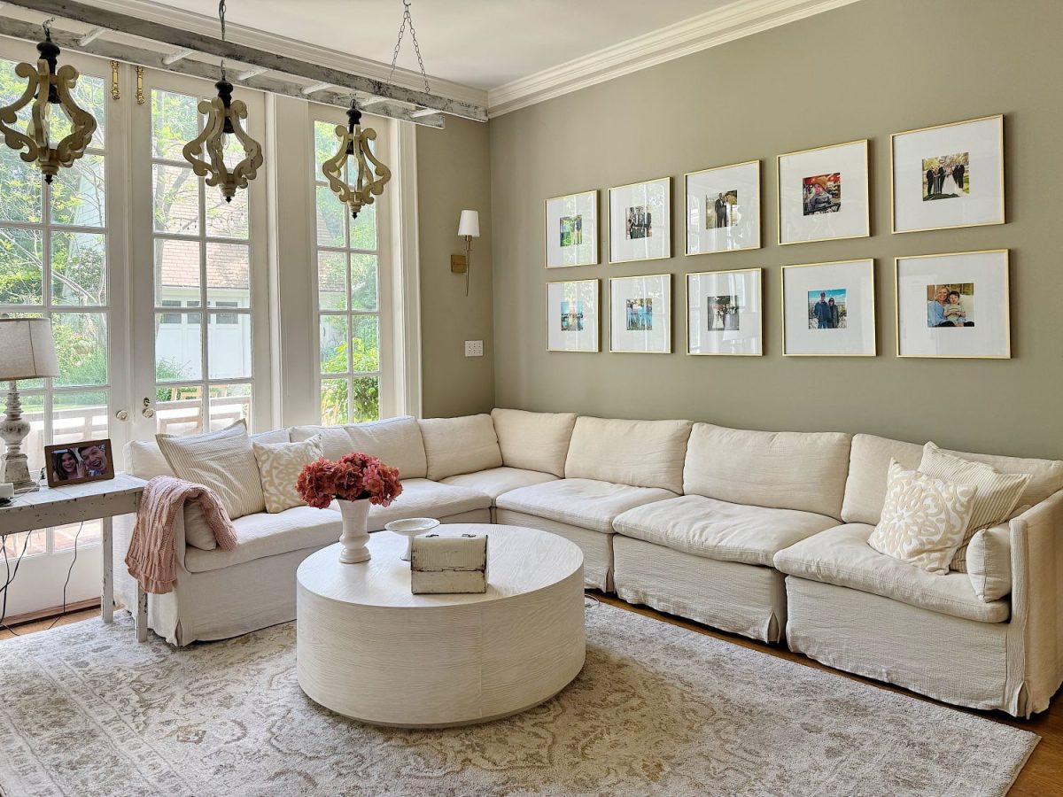 Bright living room with a large white sectional sofa, round coffee table, wall art, and floor-to-ceiling windows letting in natural light.
