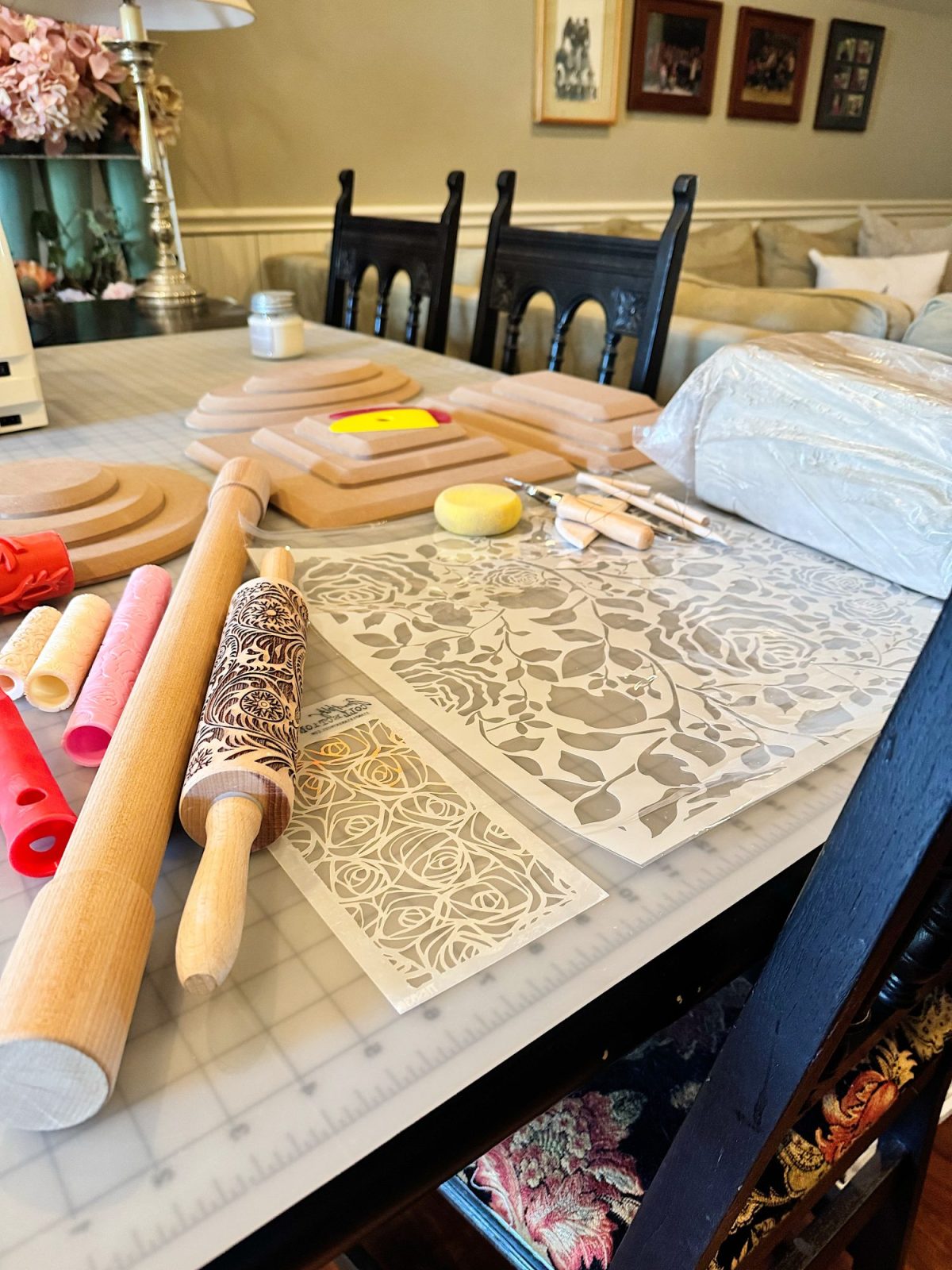 A tabletop displays rolling pins, textured rolling pins, stencils with floral patterns, sculpting tools, and cutting boards, set up for a craft or baking project.