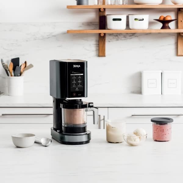 A Ninja coffee maker sits on a kitchen counter next to a glass of milk, a jar with pink liquid, a bowl with ice cream scoops, a measuring cup, and a spoon.