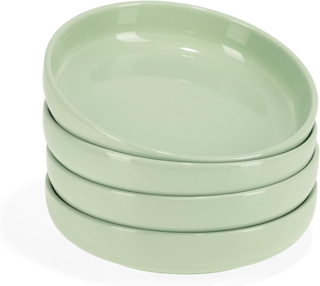 A stack of four light green ceramic shallow bowls, perfect for serving healthy summer recipes, placed one on top of another on a white background.