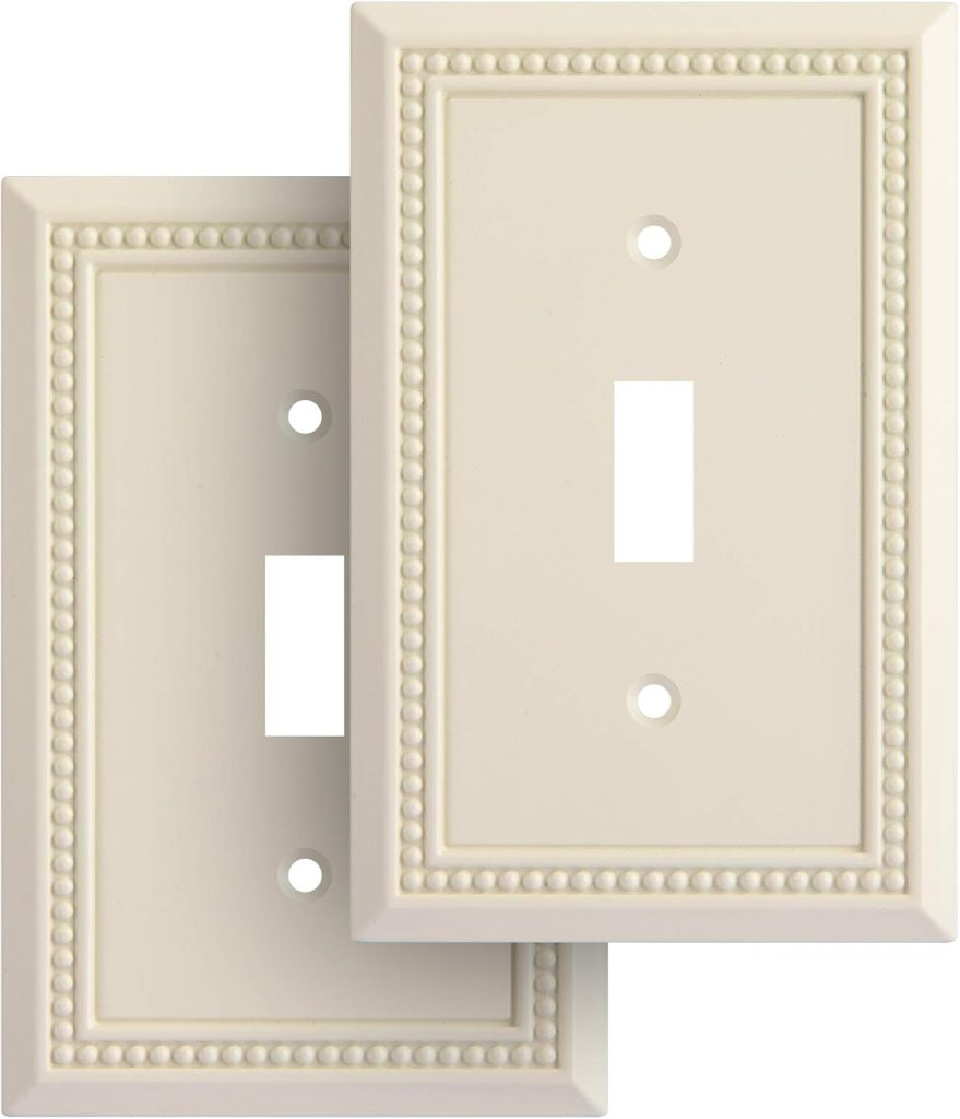 Two ivory-colored decorative light switch plates with a beaded border design evoke that classic Nancy Meyers aesthetic, with one plate slightly overlapping the other.