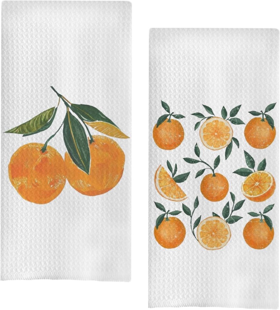 Two white kitchen towels featuring orange fruit illustrations; one towel shows two whole oranges with leaves, while the other displays multiple oranges and orange slices with leaves in a cheerful creamsicle-inspired palette.