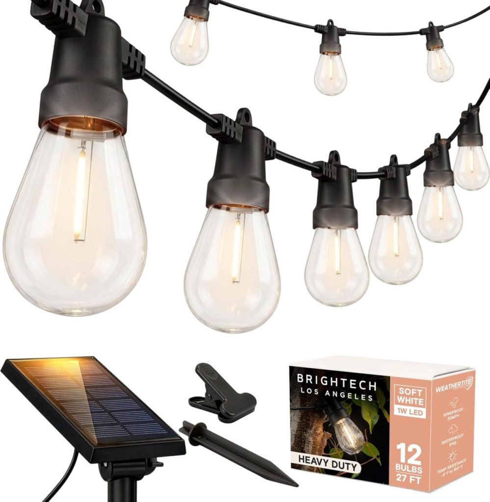 String of clear, teardrop-shaped LED bulbs hanging outdoors, perfect for a backyard dinner party, powered by a solar panel; product box labeled “Brightech” and “12 bulbs, 27 ft, heavy duty.”.