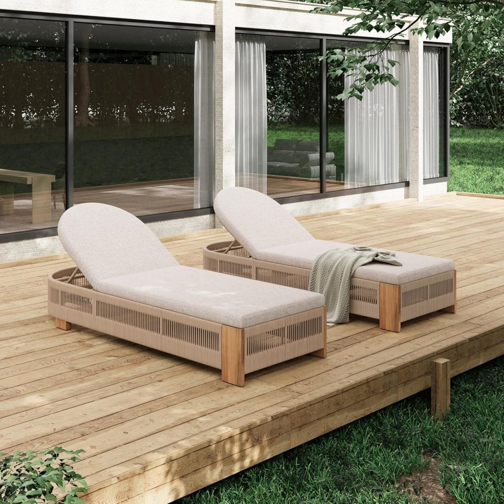 Two cushioned lounge chairs with wooden frames, chosen by top interior designers, are placed side by side on a wooden deck outside a modern house with large glass windows. A light blanket is draped over one chair.