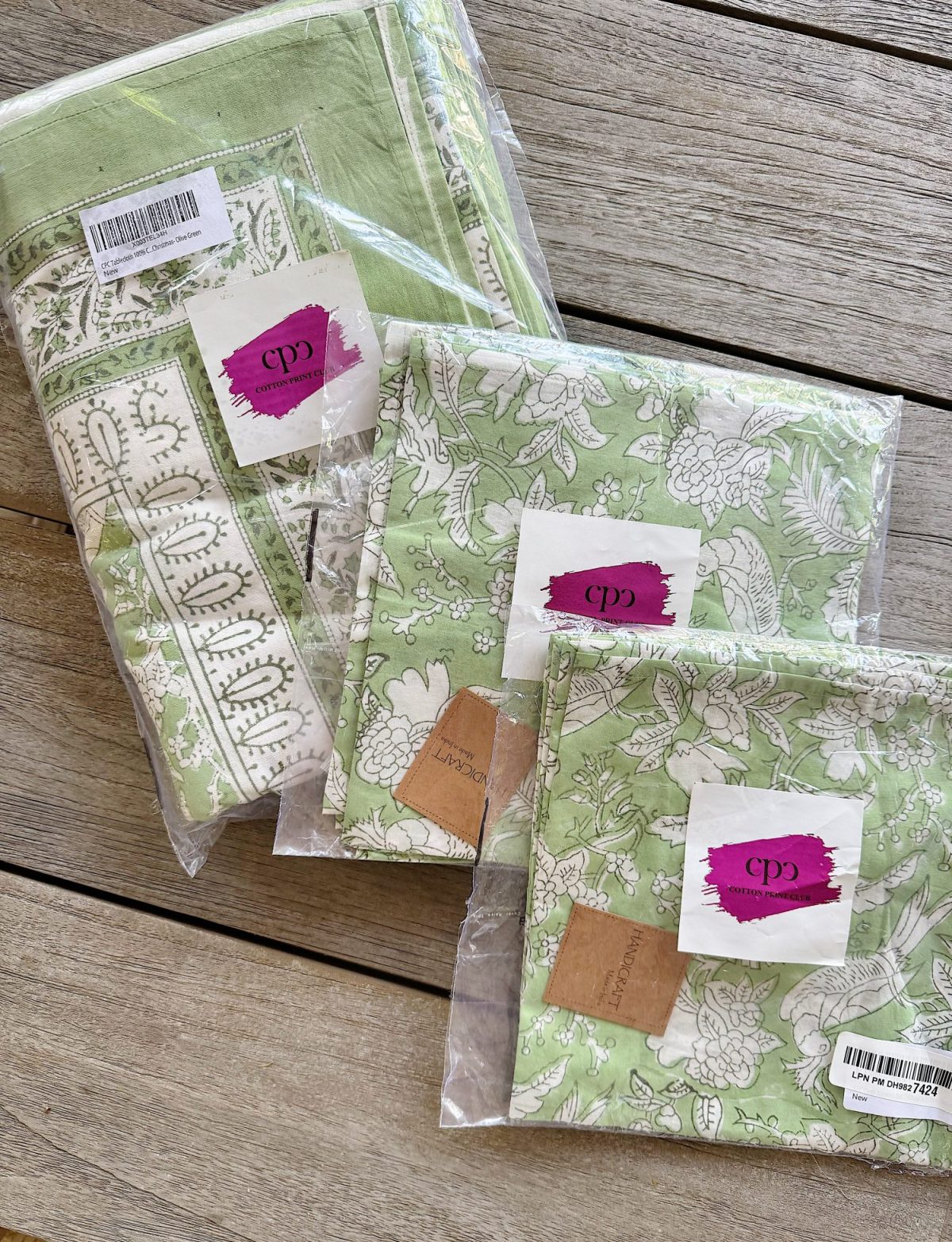 Three green and white floral-patterned fabric packs are displayed on a wooden surface, each wrapped in clear plastic with a label marked "cp.