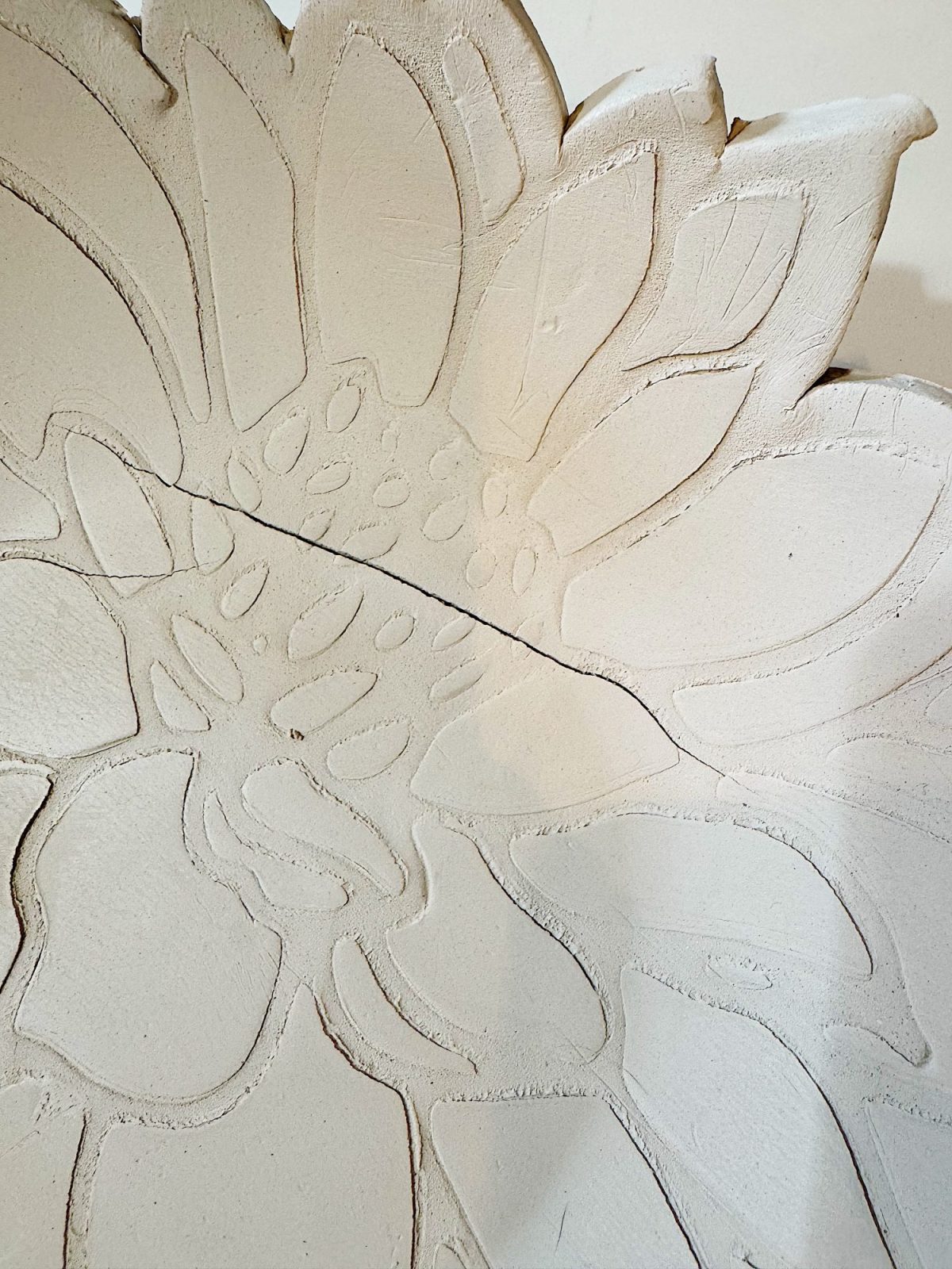 A close-up of a clay plate with a carved sunflower design and a visible crack running through the center.