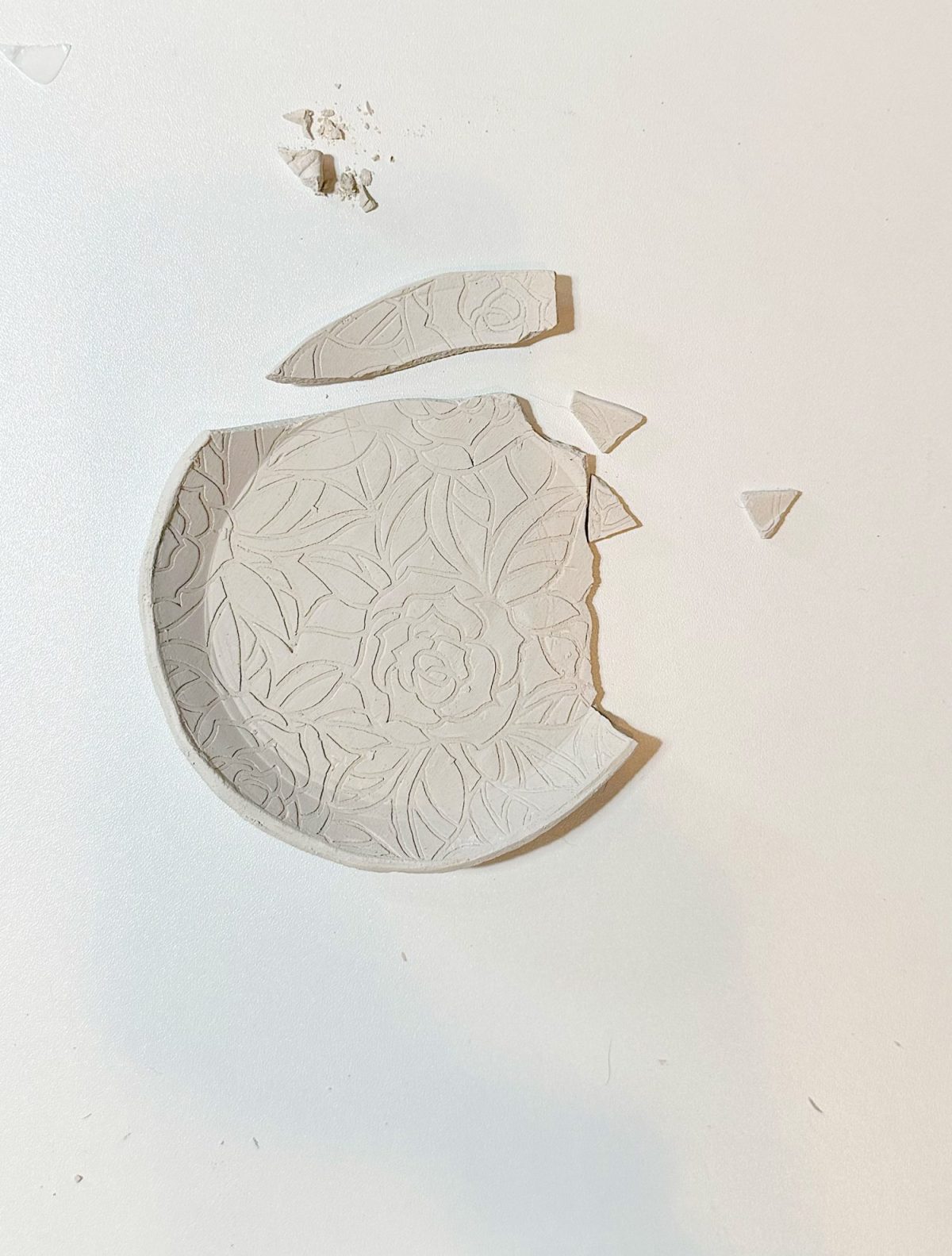 A round, floral-patterned ceramic plate is broken into several pieces on a white surface.