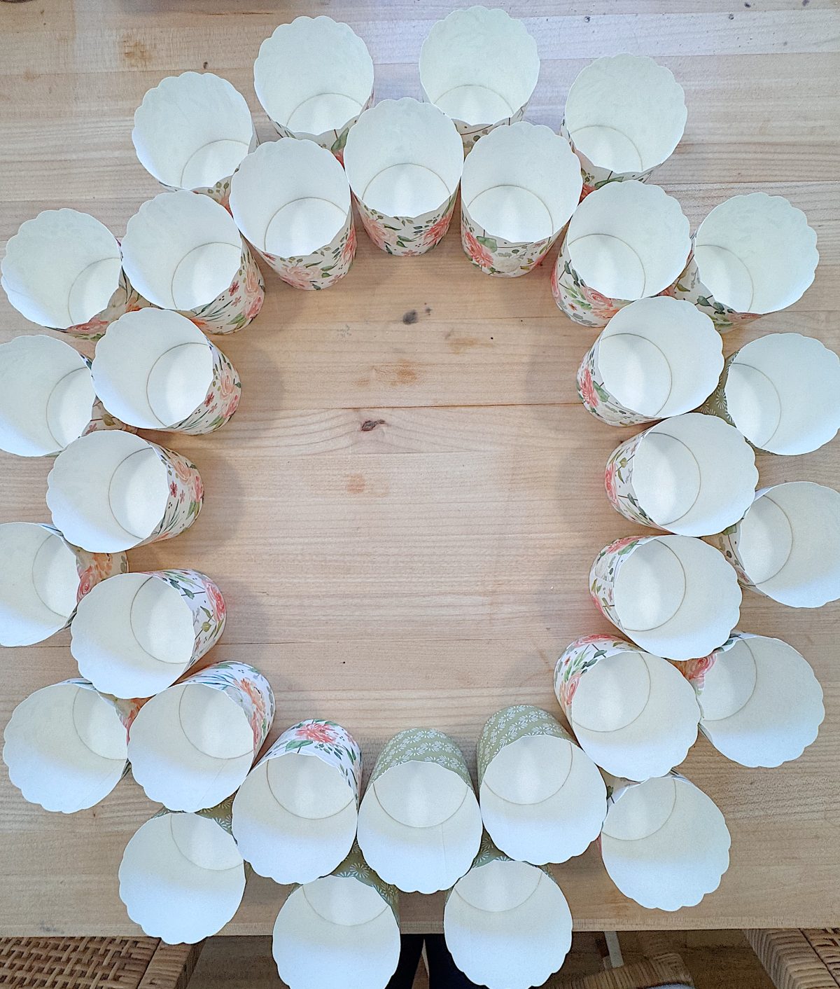 A circle of paper cups with floral patterns arranged on a light wooden table, viewed from above.